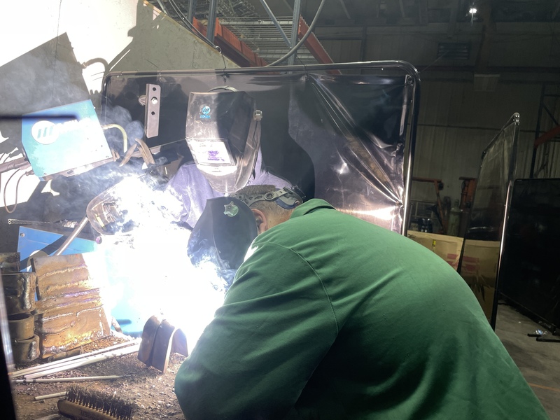 Man welding as younger man looks on