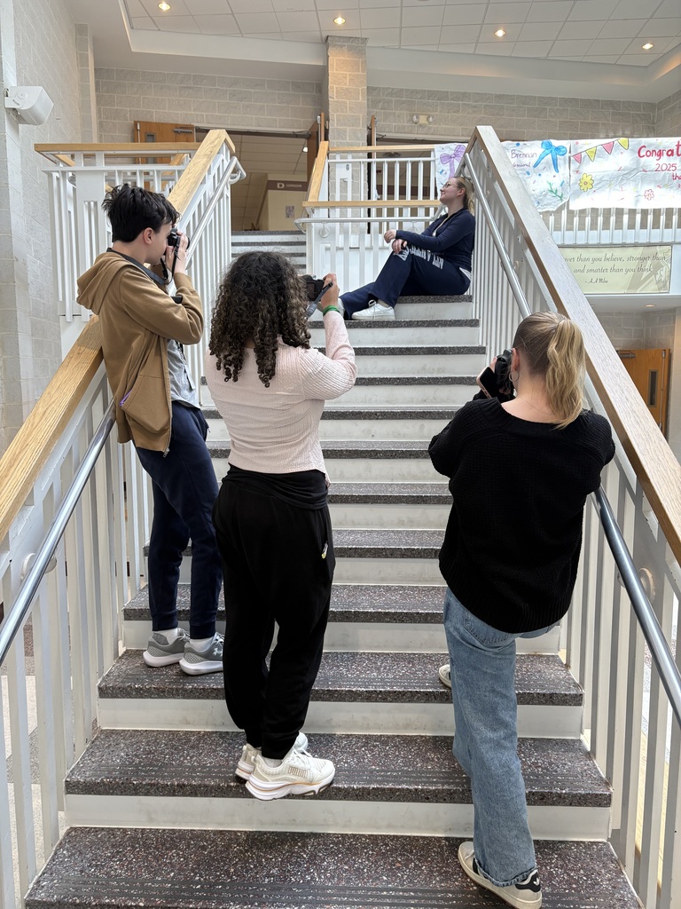 Four people taking photos, one seated on a staircase. Stairs have marble steps and white railings.
