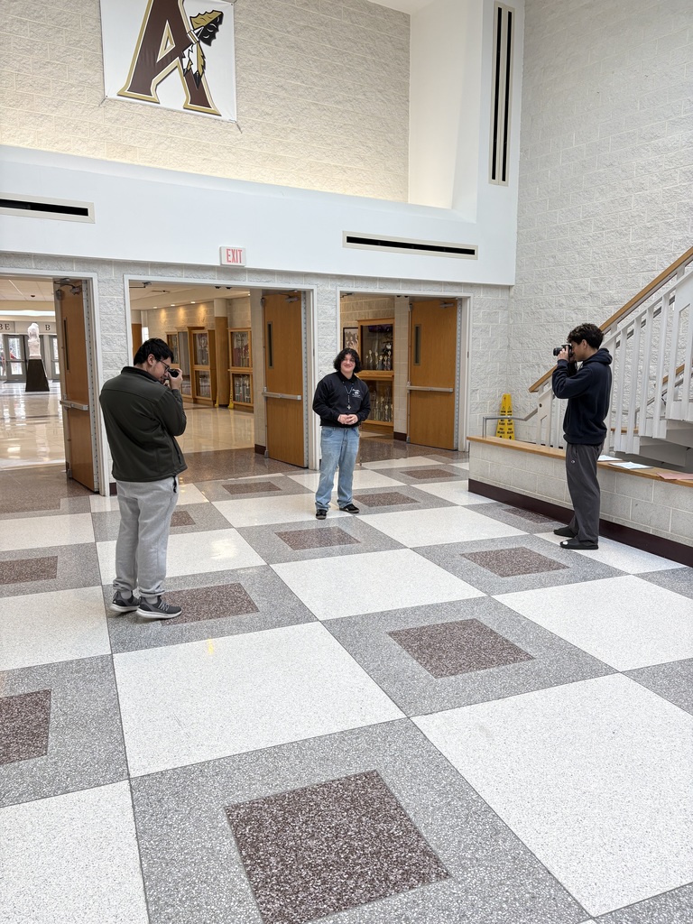 Three individuals in a hallway with a checkered floor, taking photos. One holds a camera, while two others face a staircase.