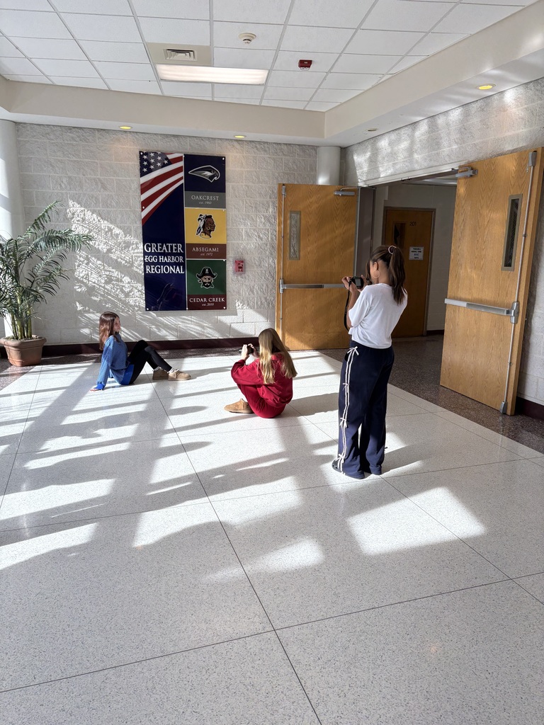 Three individuals in a hallway; one takes photos while two others pose on the floor.
