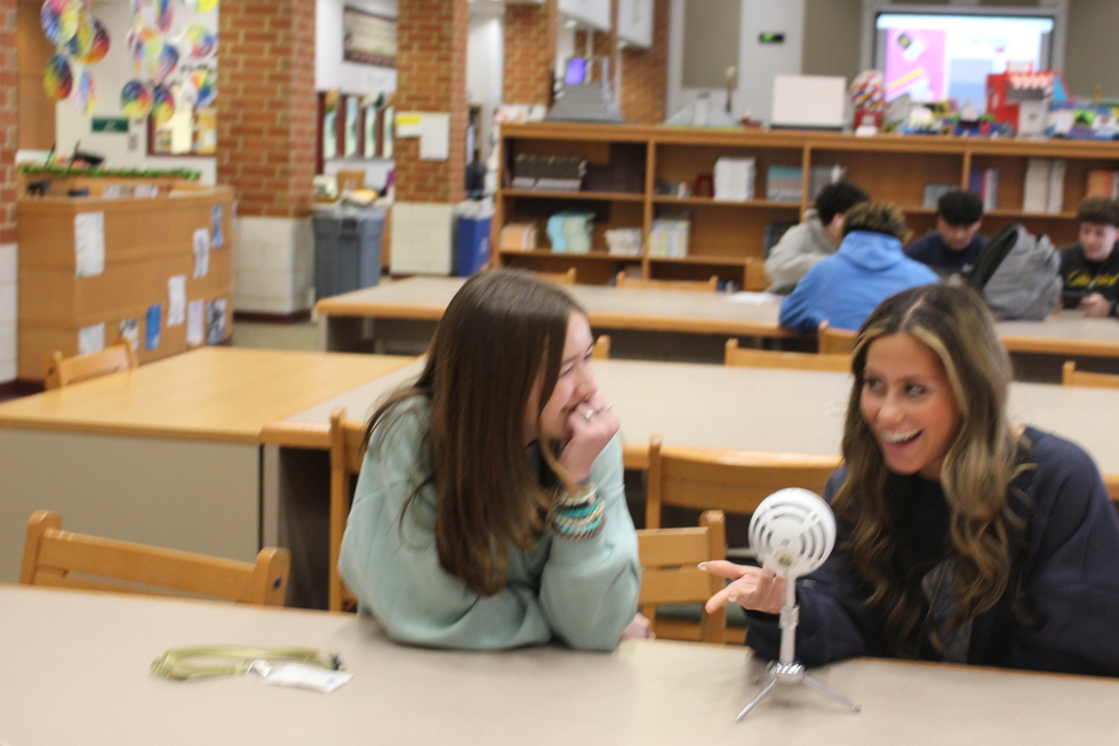 Two girls talk over microphone.