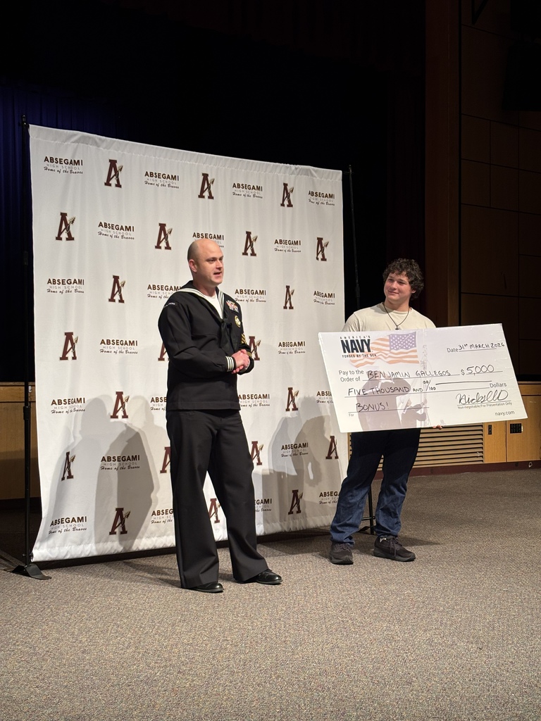Two individuals stand on stage, holding a large check, with a large banner behind them displaying 'A' letters.