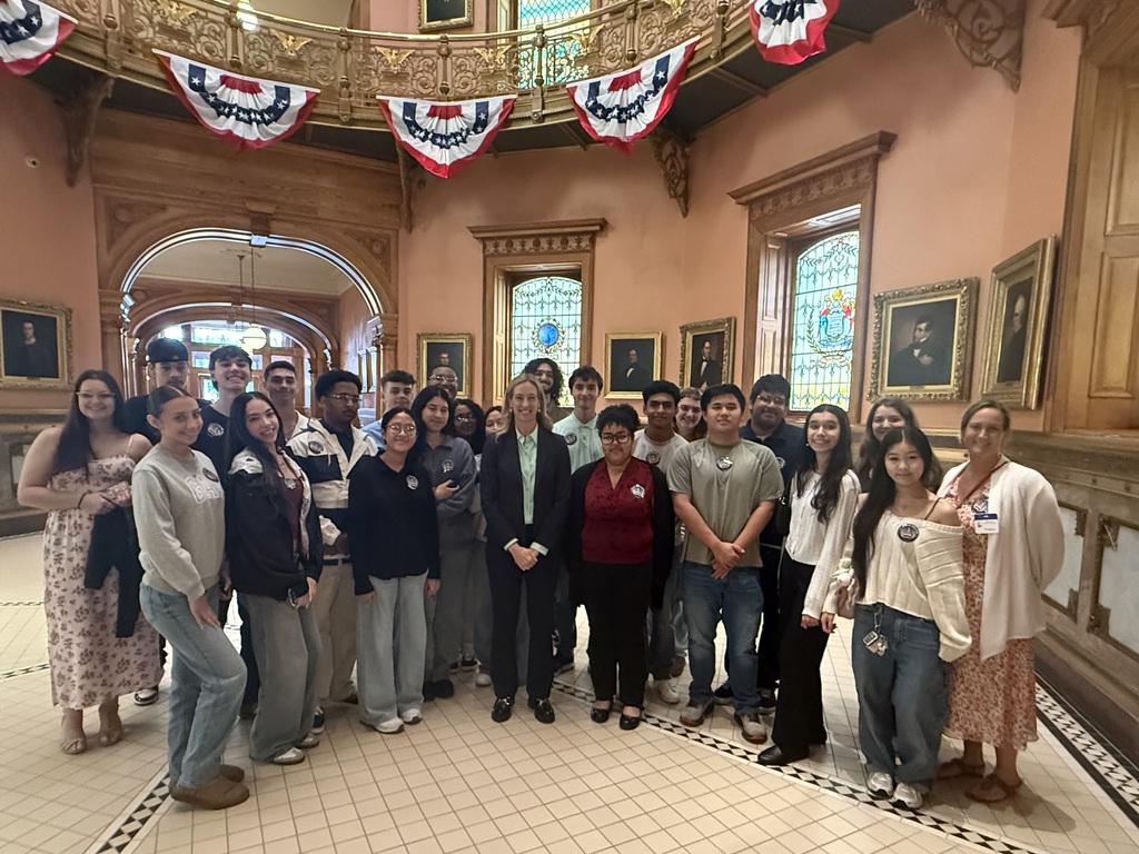A group of people stand together in a building with flags, ornate ceilings, and decorative picture frames.