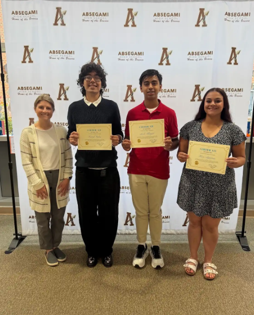 Four individuals standing together holding certificates. A white backdrop with text and logos.