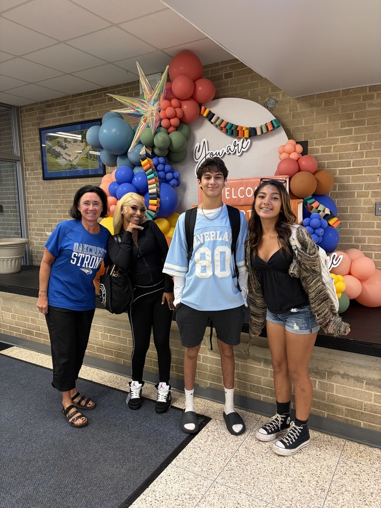 Four people stand next to each other. A decorative arch of colorful balloons is behind them.