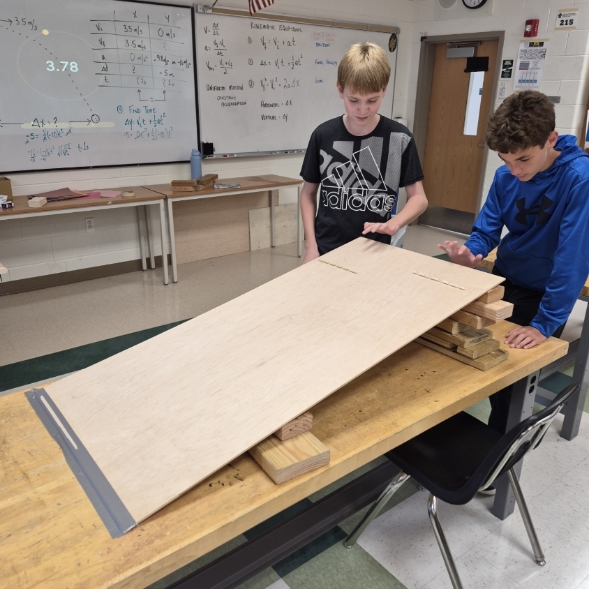 Two people work on a large piece of wood, one standing and the other bent over.