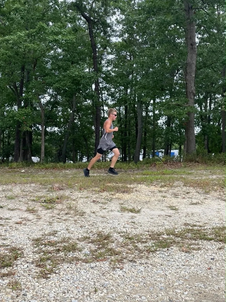 A person wearing a gray shirt and black shorts runs on a gravel path with trees in the background.