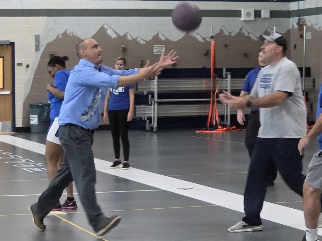 Several people are playing a ball game indoors. One man throws a ball to another man.