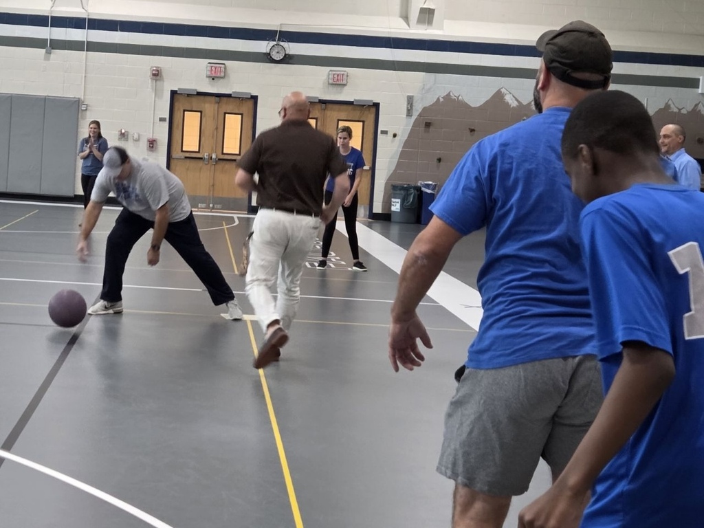 A group of people in blue and white shirts play a game with a ball indoors.