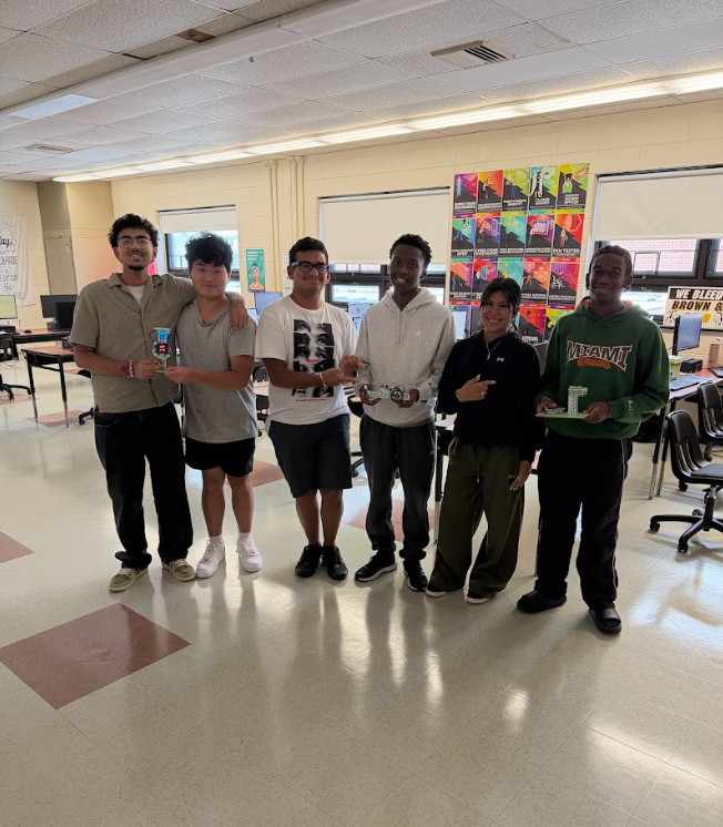Six individuals in a classroom with awards in their hands, smiling and posing for a photo.