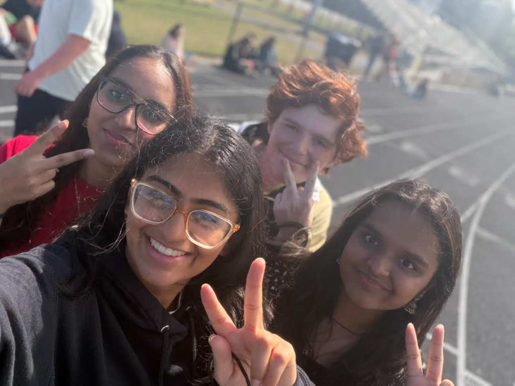 Four people pose with peace signs on a track, one making a peace sign with both hands.