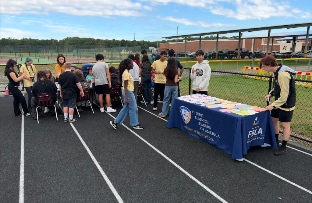 A group of people are gathered on a track with a table displaying a banner with blue background.