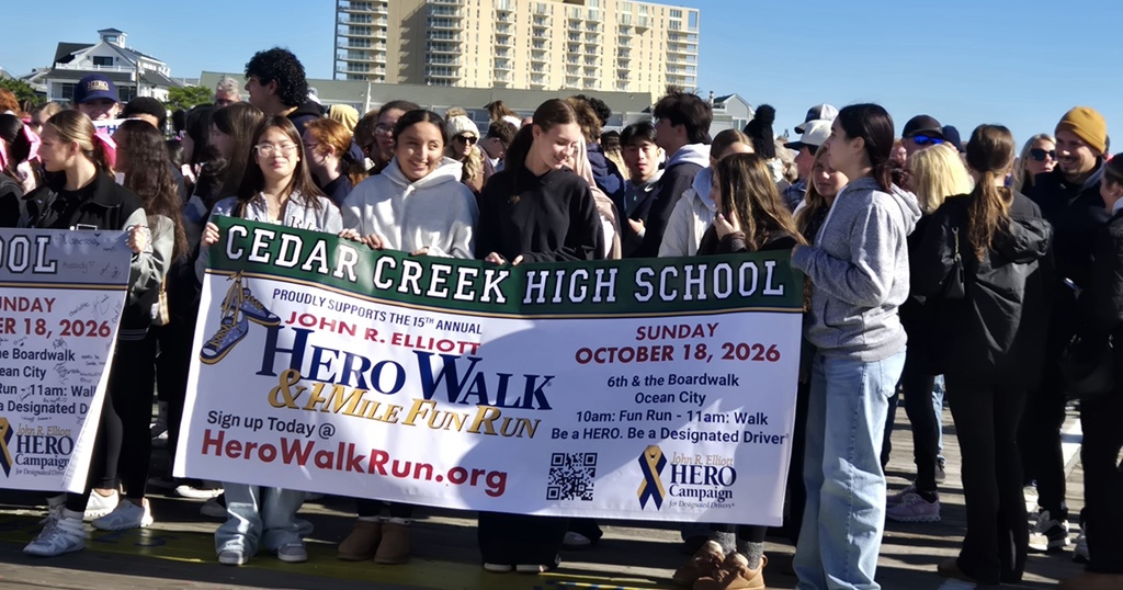 People holding a green banner reading Cedar Creek High School Hero Walk, standing in a crowd.