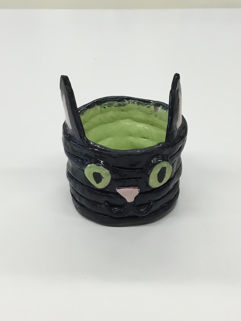 A black, green, and pink decorative item resembling a cat on a white surface.