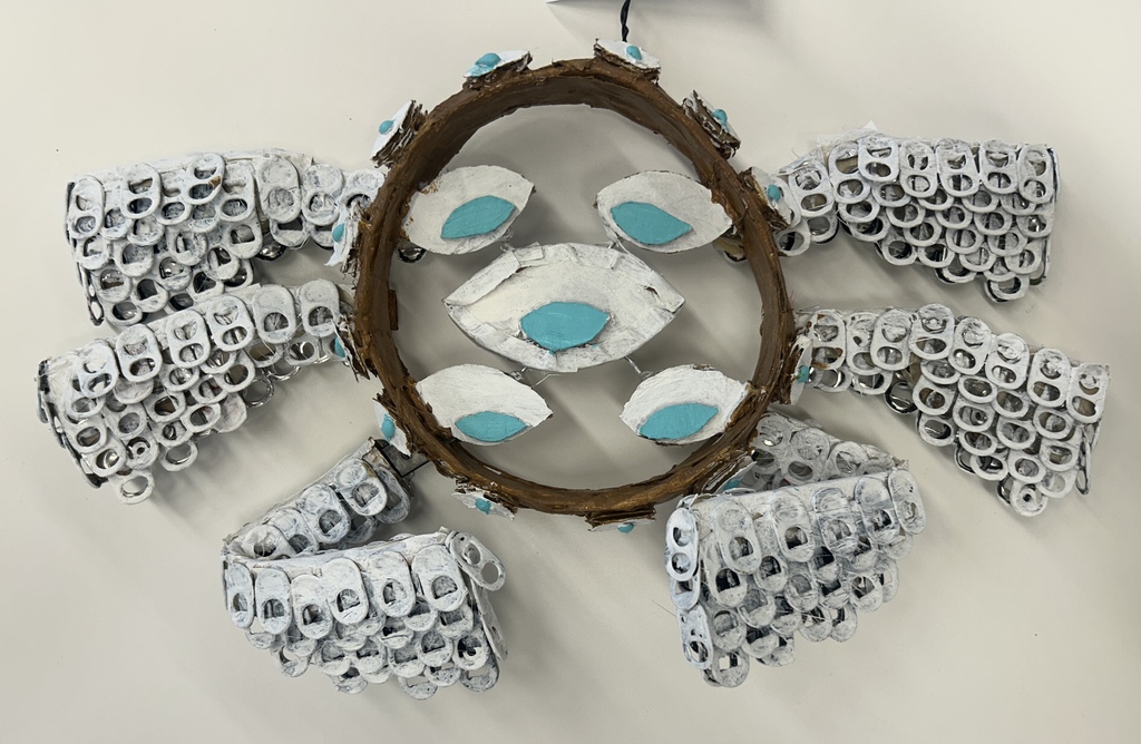 A circular craft made of can tabs and turquoise stones hangs on a wall.