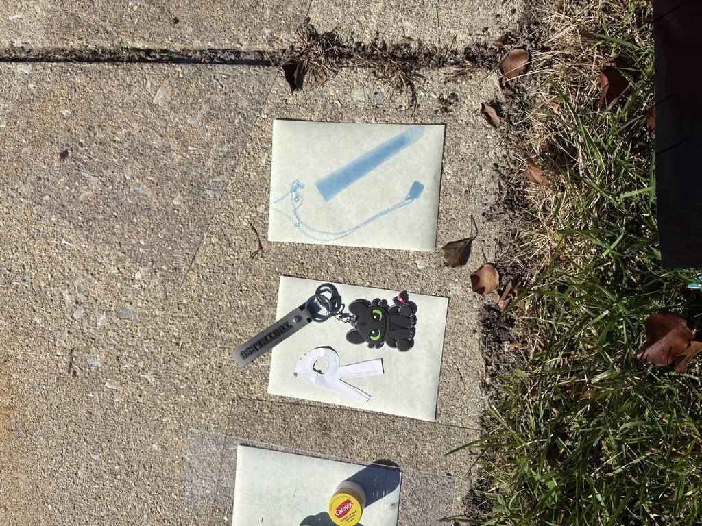 Three white papers on concrete, one with a blue line, another with a razor and a small black toy, third with a yellow sticker.