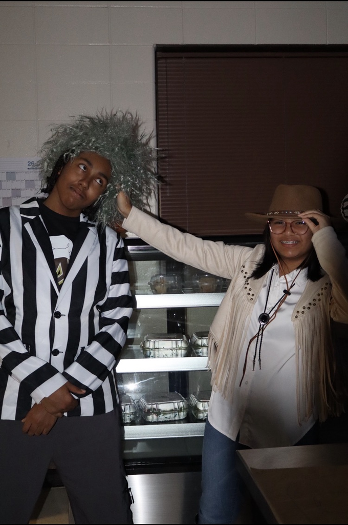 A person with a wig and a striped jacket stands next to a person in a hat.