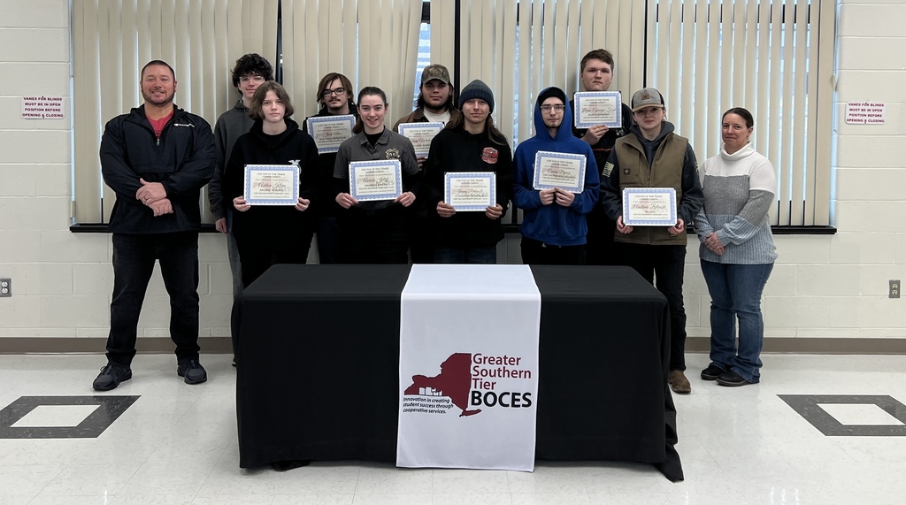 Students holding certificates standing behind a table.