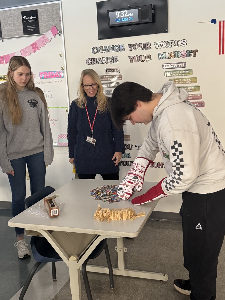 One student learning to pick things up with oven mits on his hands while an instructor and peer watch.
