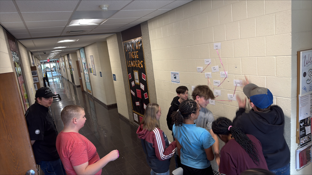 Students working together on a chain of note cards on a wall.