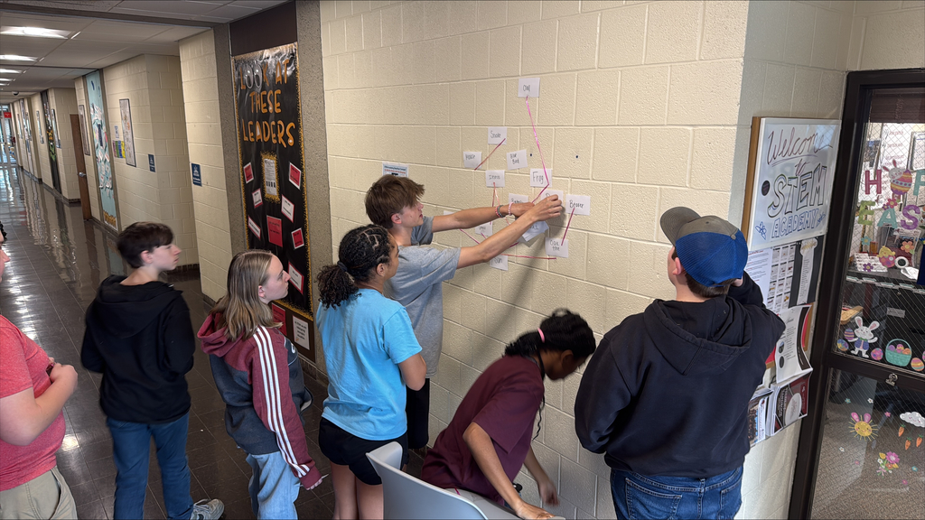 Students working together on a chain of note cards on a wall.