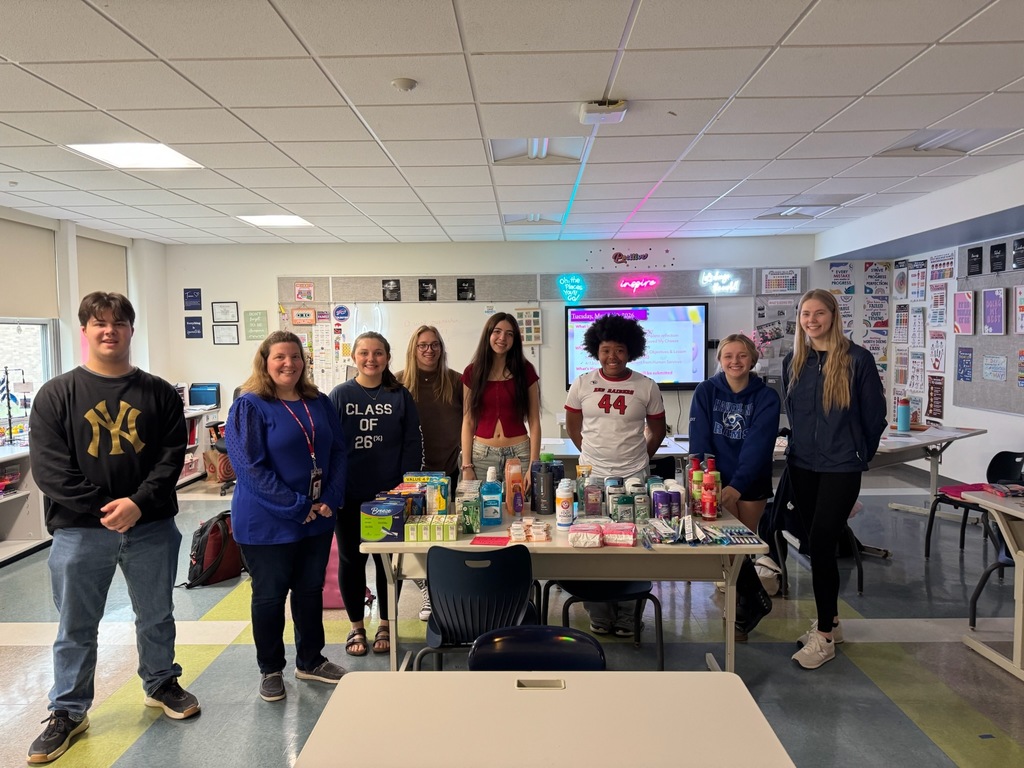 A classroom of students standing around a table of hygiene products.