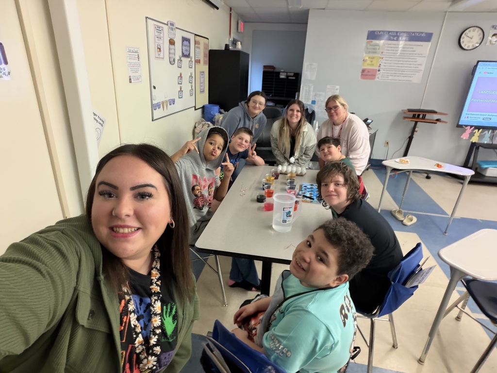 Classroom of students and staff smiling at a camera around a table of eggs.