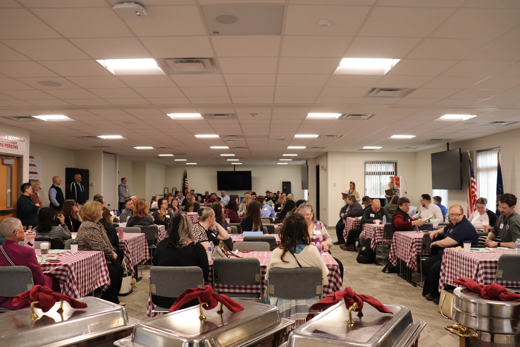 A room of business and industry partners listening to the welcome message while sitting at tables.