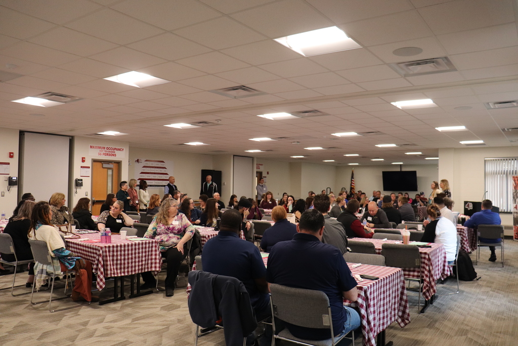 A room of business and industry partners listening to the welcome message while sitting at tables.
