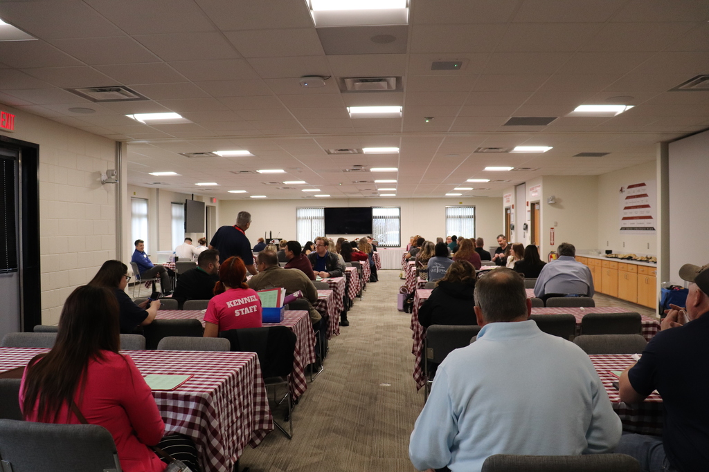 A room of business and industry partners listening to the welcome message while sitting at tables.