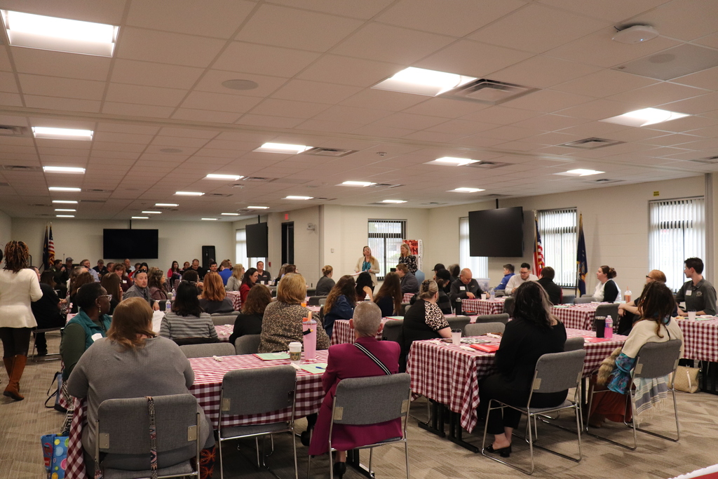 A room of business and industry partners listening to the welcome message while sitting at tables.