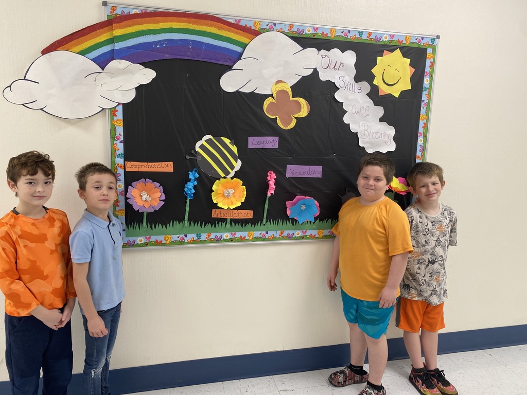 Four students standing in front of a spring themed bulletin board.