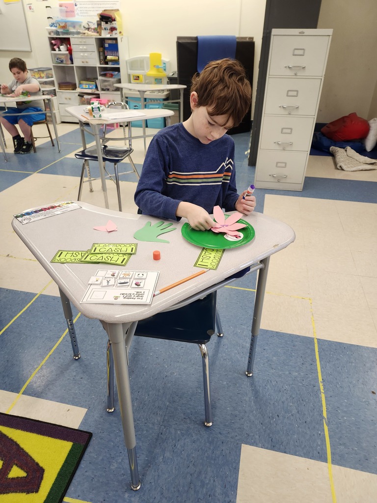A student at a desk making a lily pad out of paper with glue.