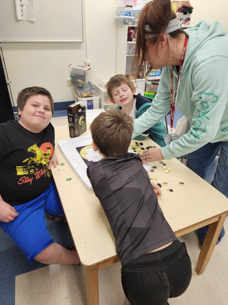 three students and a teacher putting a puzzle together