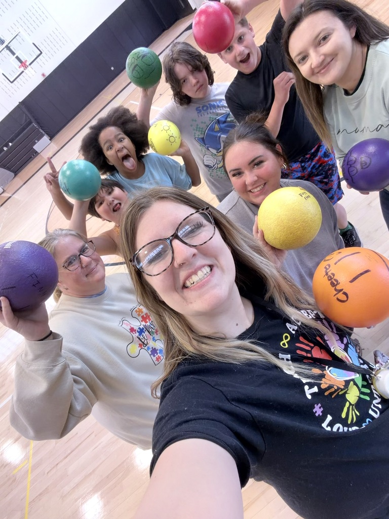 Students and staff smiling and holding a ball in the gym