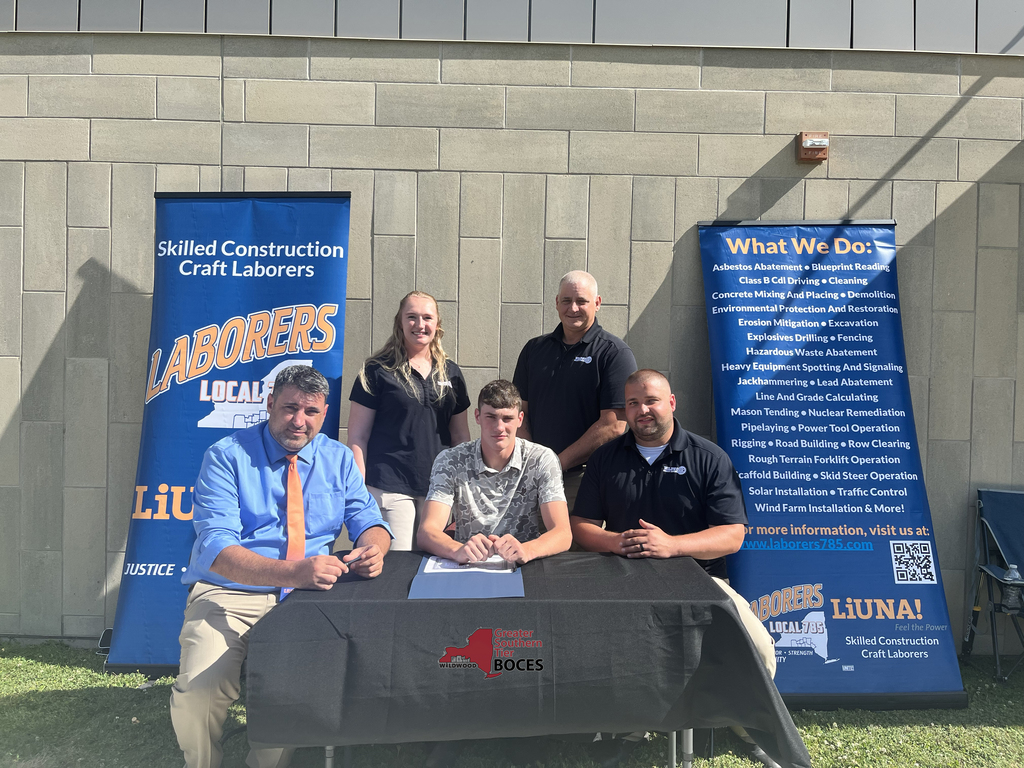 Student, teachers and business and industry representative behind a table at signing event.