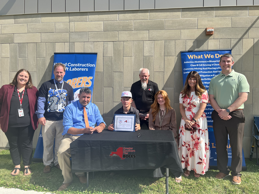 Student, teachers, staff and business and industry representative behind a table at signing event.