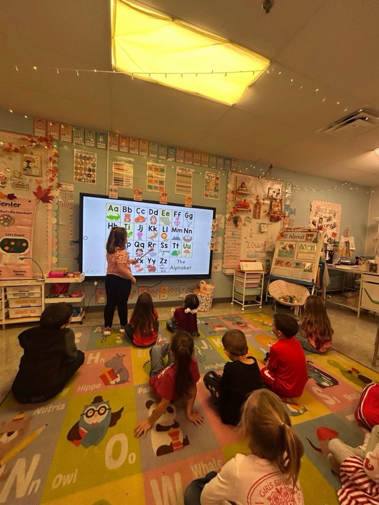 A class of students sitting in the floor practicing their alphabet