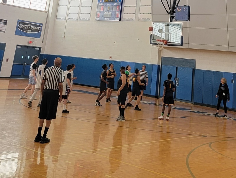 the referee stands with his back to the camera watching the players in the gym