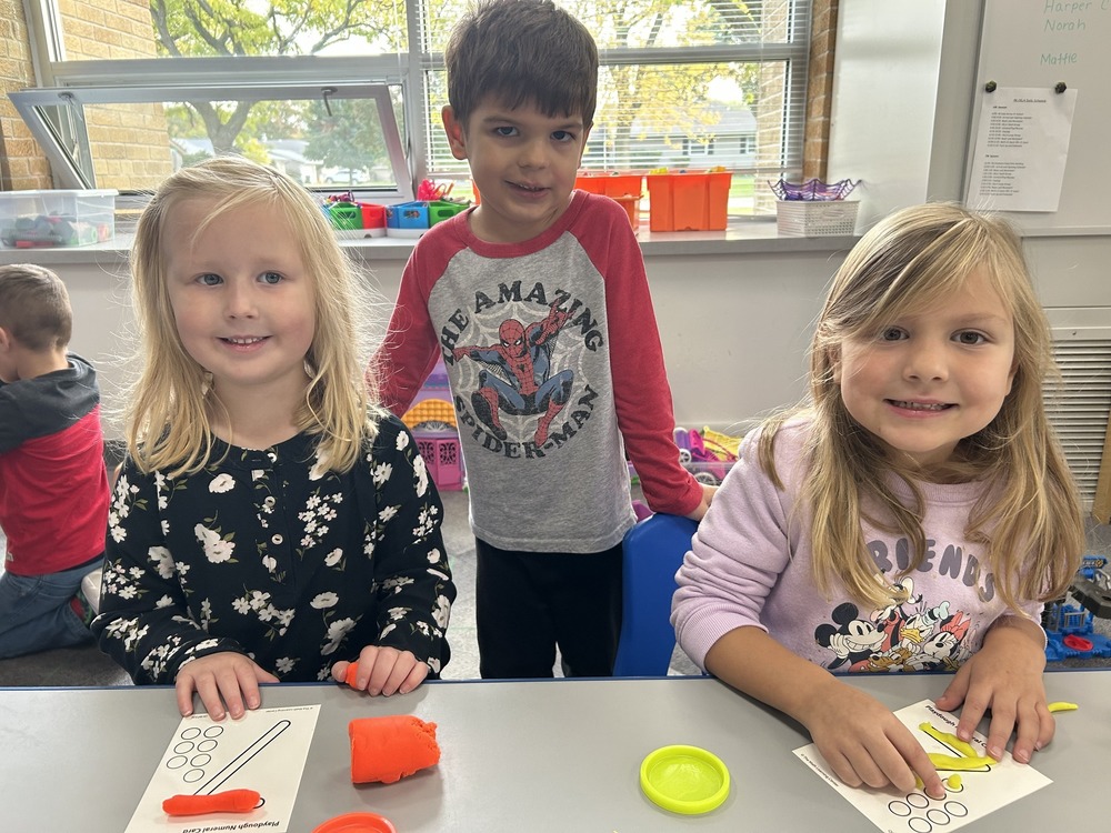 Three students smiling at camera with playdough