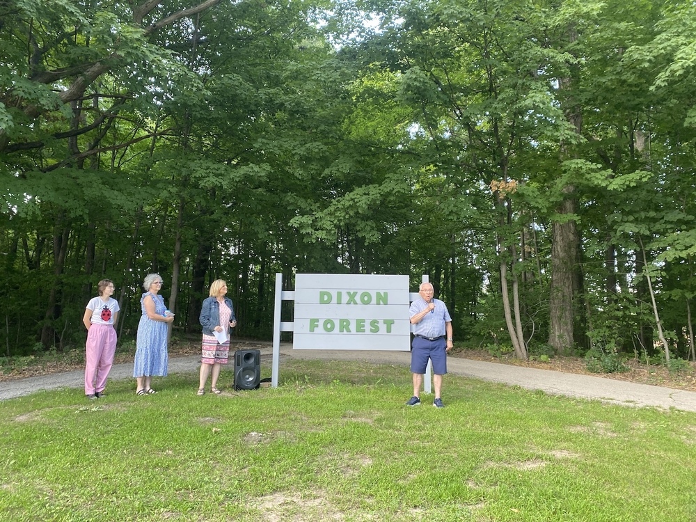 People standing by a sign that reads Dixon Forest. One person is addressing the crowd.