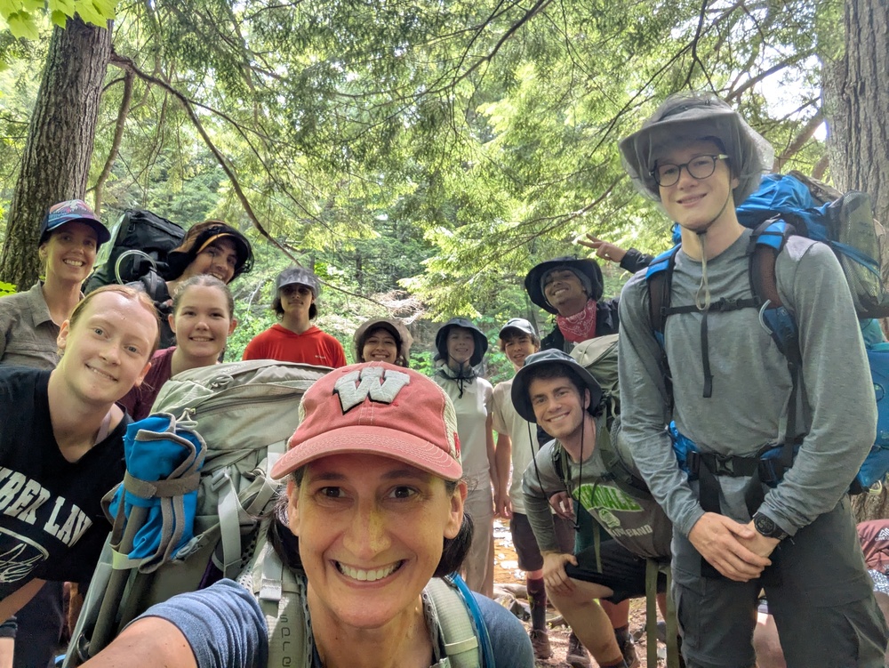 12 people smiling at the camera standing in the woods