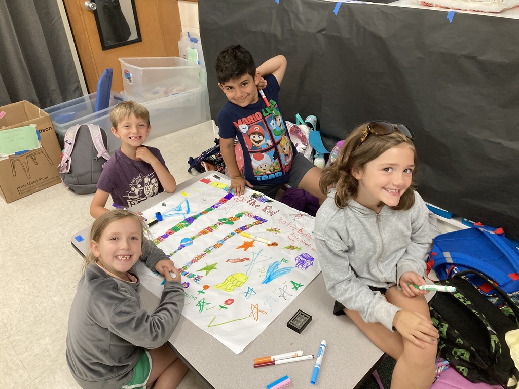 Four smiling students with markers and a poster board working on a game.