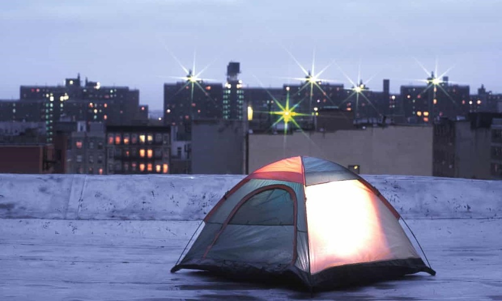 A tent on a rooftop in a city. Buildings in the background.