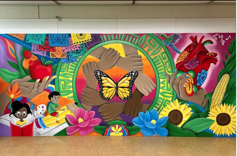 Mural on a school wall with students, flowers, butterflies and interlinked hands.
