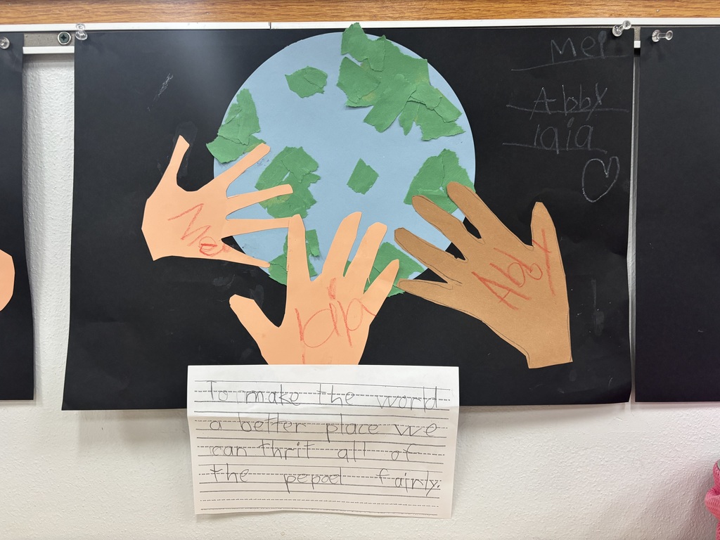 Students handprints touching a light blue globe posted on a black piece of paper and writing how to make the world better by treating people fairly. 