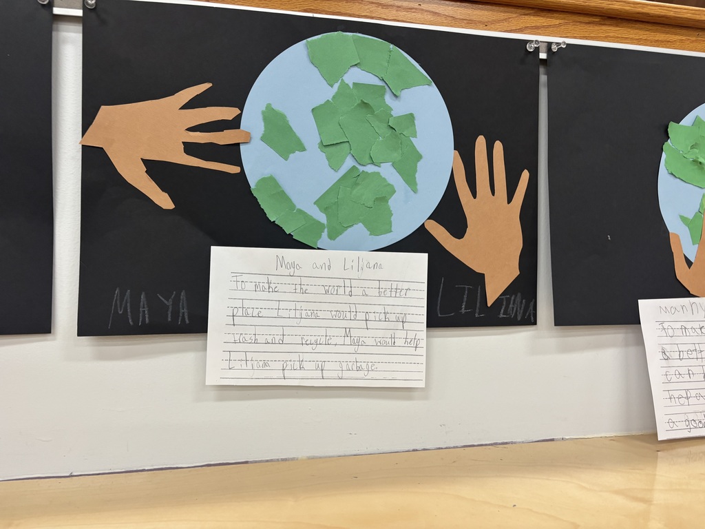 Students handprints touching a light blue globe posted on a black piece of paper and writing how to make the world better by helping with the wash and picking up garbage.