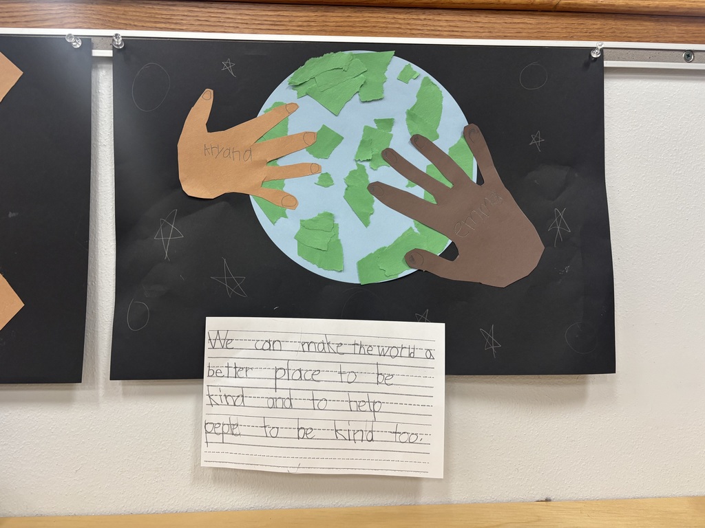 Students handprints touching a light blue globe posted on a black piece of paper and writing how to make the world better by being kind and teaching people how to be kind.