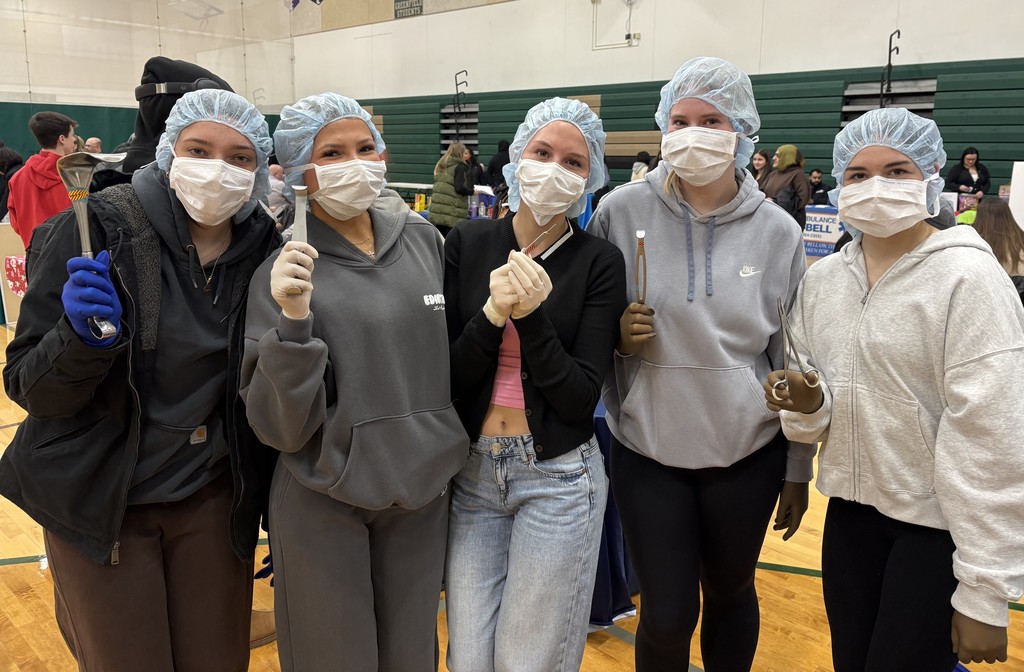 A group of five individuals in a gymnasium wearing surgical caps and masks, holding surgical instruments.