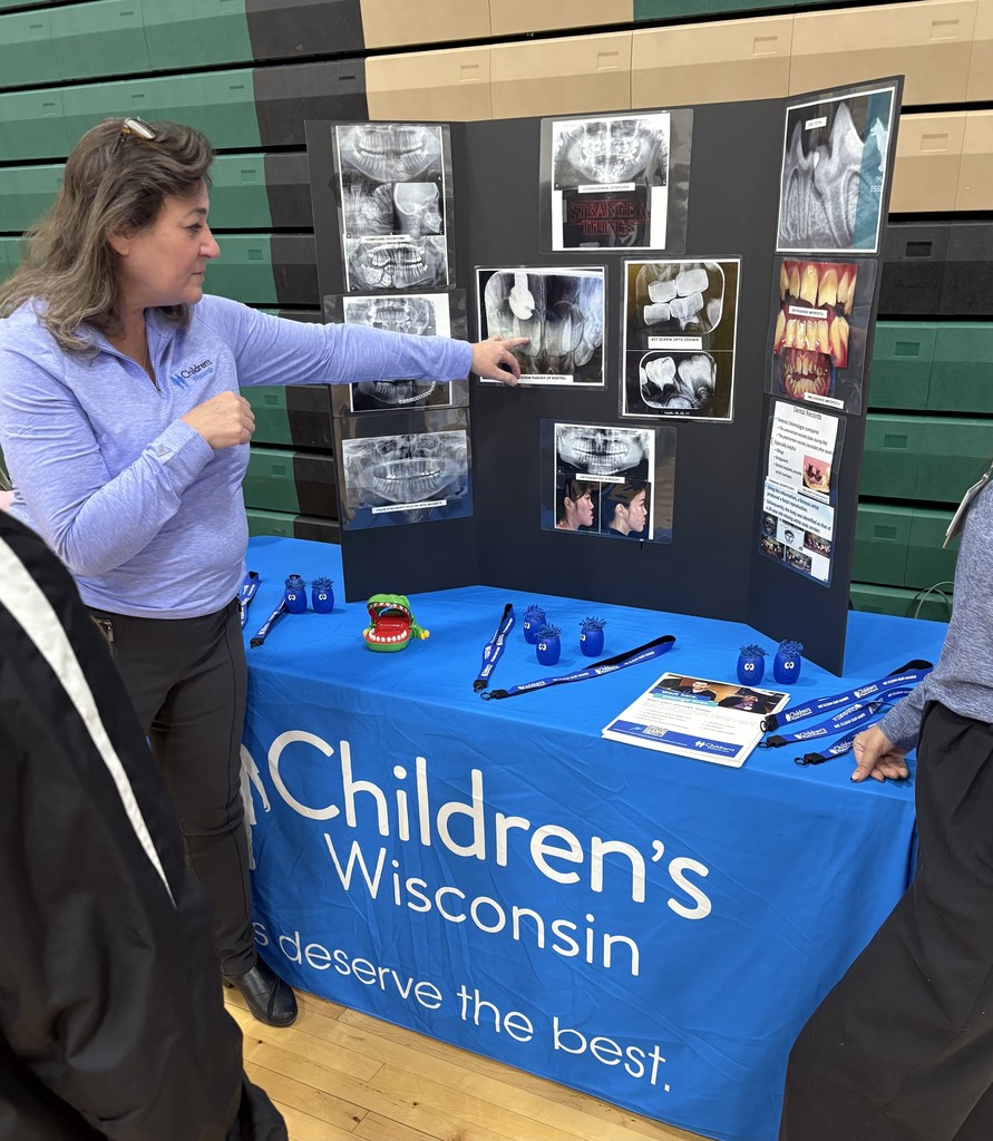 A woman points to x-ray images on a display board at a Children's Wisconsin booth with blue tablecloth.